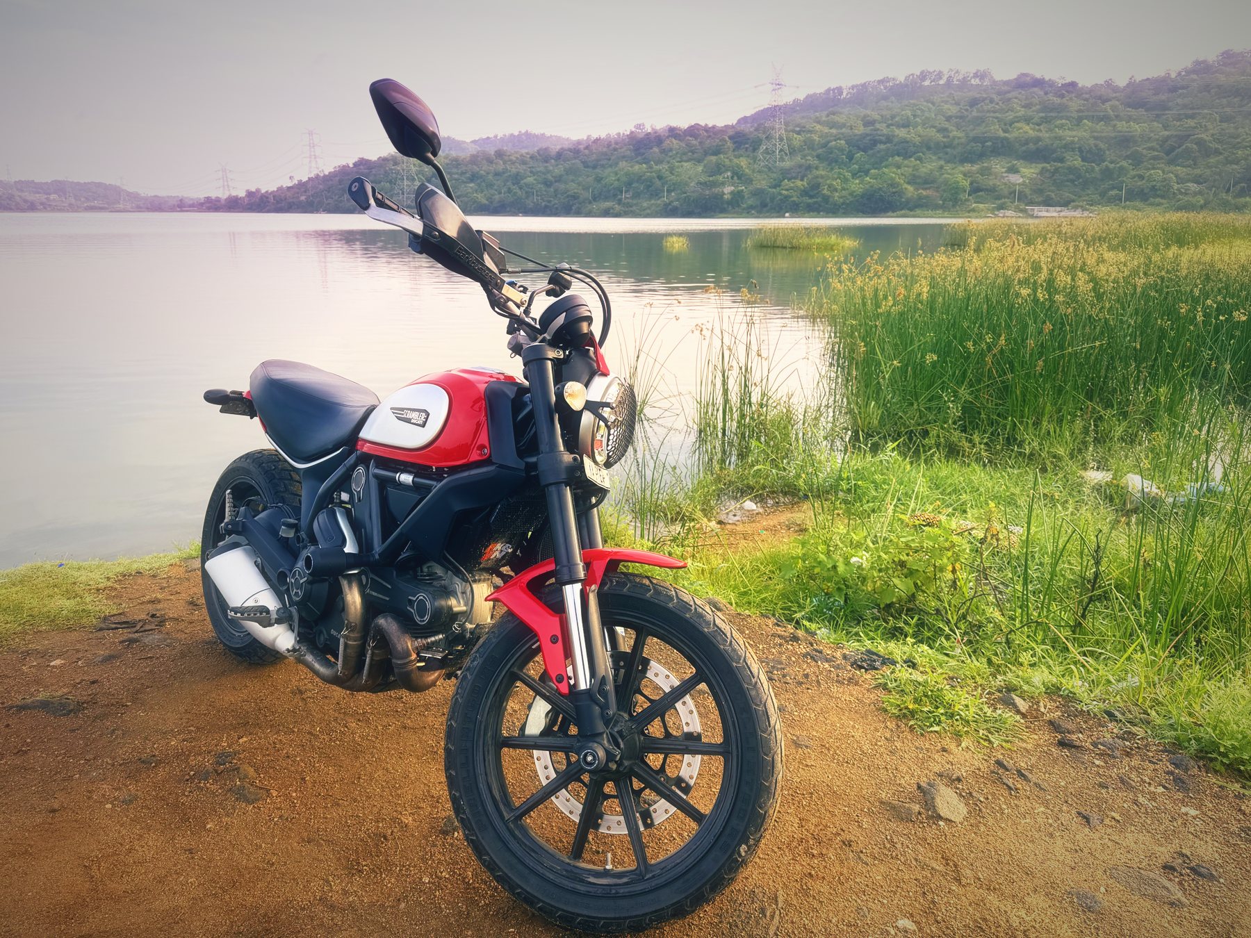 The Scrambler beside tall reeds, with power pylons along the hills