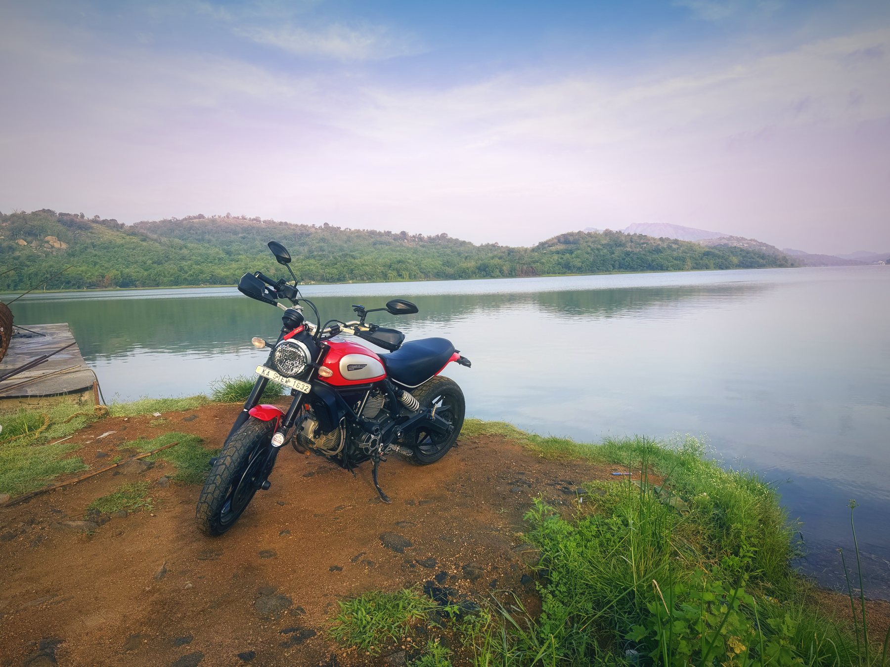 The Scrambler parked on red earth at the waterline, hills across the reservoir